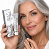 Mature model with silver hair and professionally defined brows holding RefectoCil No. 1.1 Graphite eyebrow and eyelash tint with a dual-ended brow brush